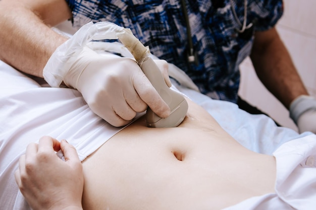 Dispositivo de escáner de ultrasonido en la mano de un médico profesional que examina a su paciente haciendo un escaneo de ultrasonido abdominal embarazo temprano para una niña