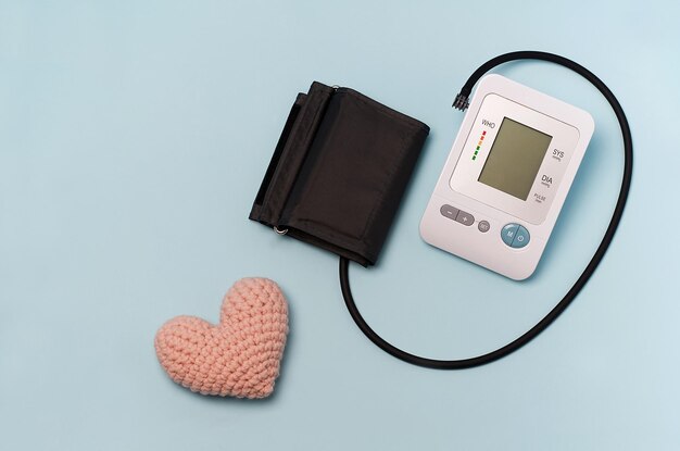 Un dispositivo para medir la presión de un tonómetro sobre un fondo médico azul y un corazón tejido