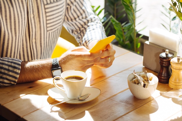 Dispositivo moderno. Close-up de um smartphone em mãos de homens enquanto está sentado à mesa no refeitório