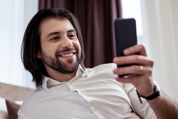 Dispositivo moderno. Retrato de um homem alegre e bonito, segurando seu smartphone moderno
