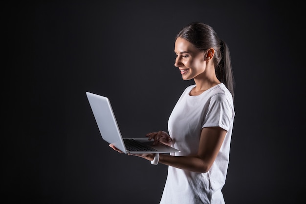 Dispositivo pessoal. Mulher bonita e atraente sorrindo e olhando para a tela do laptop enquanto segura seu gadget