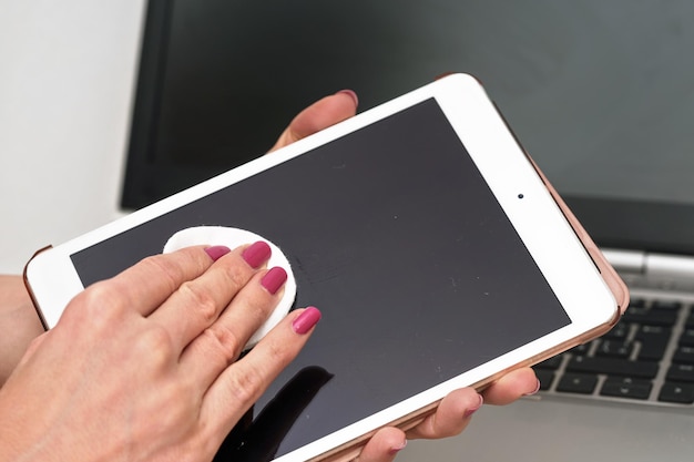 Dispositivo de tableta de limpieza de mujer con tejido de papel de algodón, pantalla negra de limpieza, detalle de cierre. Fondo de teclado portátil borroso