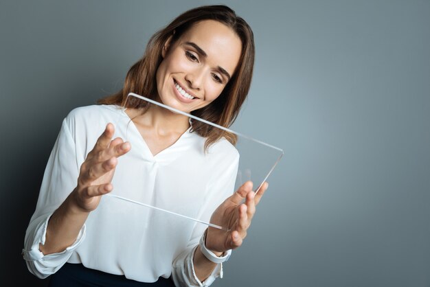 Dispositivo tecnológico. Alegre hermosa mujer agradable sonriendo y mirando la pantalla de la tableta mientras usa tecnología moderna