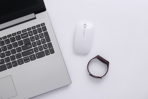 Dispositivos modernos. Laptop com mouse de pc, pulseira inteligente em fundo branco. Vista do topo. Postura plana