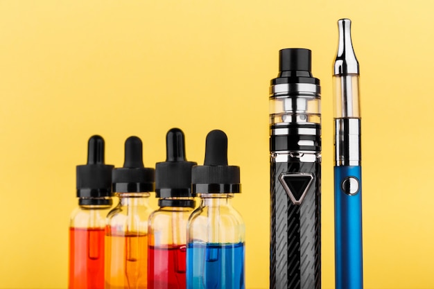 Dispositivos de vapeo y botellas con vape líquido sobre fondo amarillo.