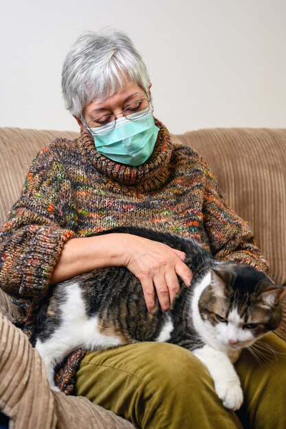 Distanciamento social do coronavírus devido a surto de pandemia. mulher idosa com máscara protetora, ficar em casa, acariciando seu gato.