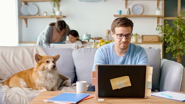 Distanciamento social. Um pai ocupado tenta trabalhar remotamente com seu filho e esposa em casa.