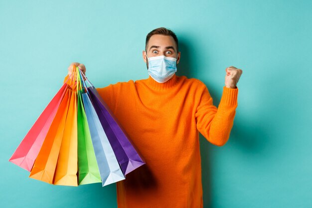 distanciamiento social y concepto de estilo de vida. Hombre emocionado en mascarilla mostrando bolsas de compras