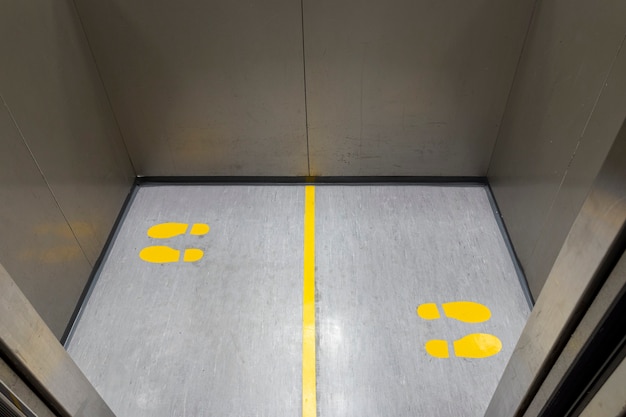 Distanciamiento social para COVID19 con señal de huella amarilla en ascensor público