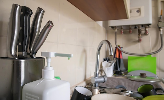 Distribuidor de esponja verde e sabonete líquido para lavar louça em pia totalmente suja com louça e utensílios de cozinha. Lavar louça na cozinha à mão com detergente e uma esponja.