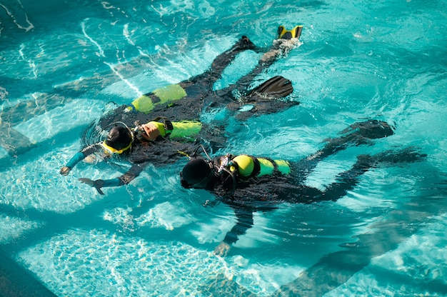 Divemaster und zwei Taucher in Aqualungen, Tauchkurs in Tauchschule. Den Menschen beibringen, mit Tauchausrüstung unter Wasser zu schwimmen, Innenpool im Hintergrund, Gruppentraining