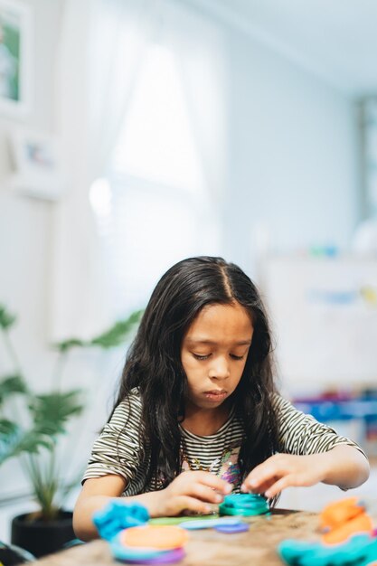 Foto diversa niña en edad preescolar en casa jugando con arcilla de modelado de colores