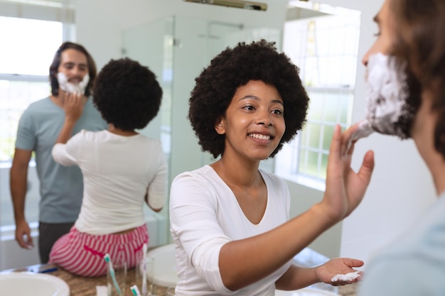 Diversa pareja parada en el baño aplicando crema de afeitar