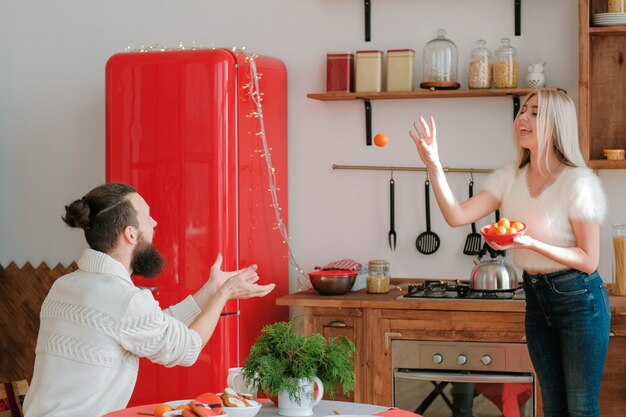 Diversão de férias de inverno. casal brincando com tangerinas na cozinha moderna, senhora jogando frutas para o namorado.