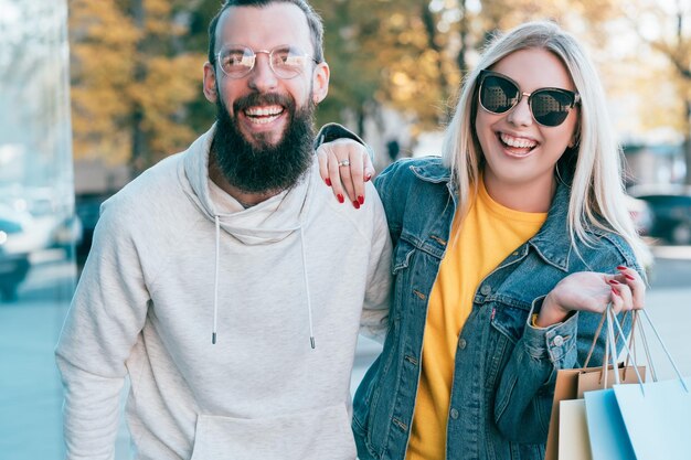 Diversão de outono Casal alegre com pacotes de compras no centro da cidade Blur queda paisagem de fundo