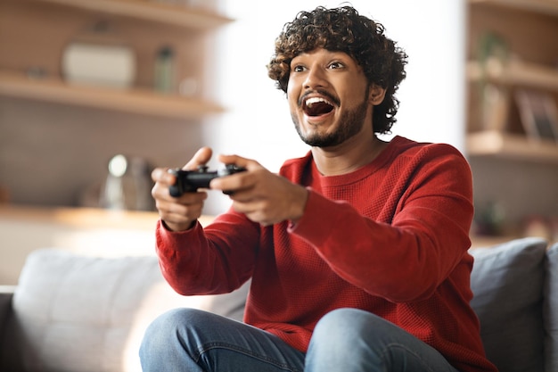 Foto diversão doméstica alegre jovem indiano jogando videogame em casa