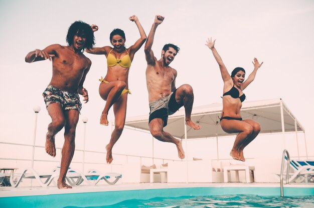 Diversão na piscina. Grupo de jovens lindos parecendo felizes enquanto pulam na piscina juntos