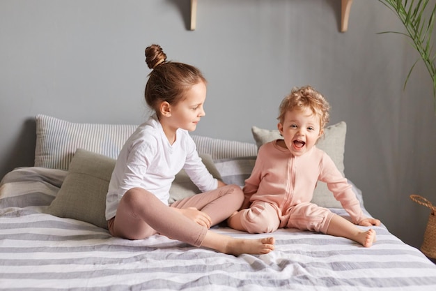 Diversão para crianças Lazer matinal para crianças Meninas bonitas e encantadoras brincando no quarto irmãs rindo na cama expressando felicidade aproveitando momentos felizes