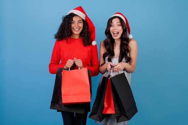 Diversas chicas emocionadas con bolsas de compras negras y rojas aisladas sobre azul