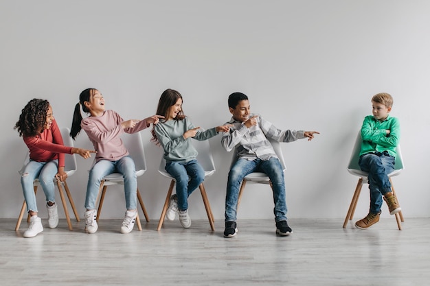 Foto diversas crianças de colegas de classe rindo apontando o dedo para estudante vítima dentro de casa