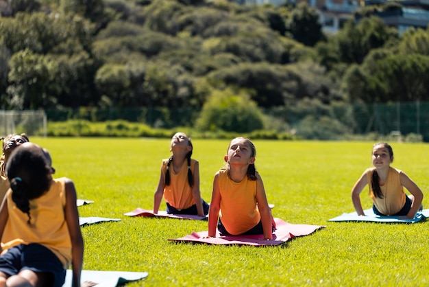 Foto diversas escolares practicando la meditación de yoga en el soleado campo deportivo de una escuela primaria