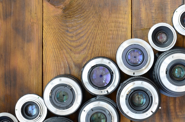 Diversas lentes fotográficas encontram-se em um fundo de madeira marrom. Espaço para texto