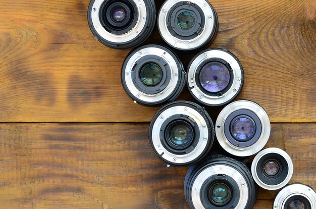 Diversas lentes fotográficas encontram-se em um fundo de madeira marrom. Espaço para texto