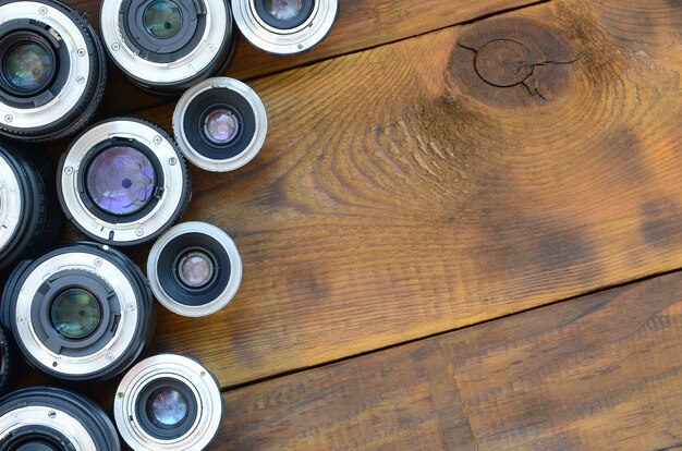 Diversas lentes fotográficas encontram-se em um fundo de madeira marrom. Espaço para texto