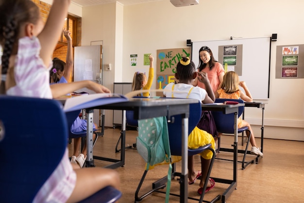 Diversas maestras y estudiantes de escuela primaria levantando las manos en clase