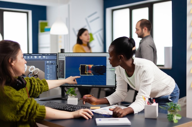 Diversas mujeres desarrolladores de software de juegos que crean una interfaz de juegos sentados en una empresa de agencia creativa de inicio apuntando a pantallas de PC