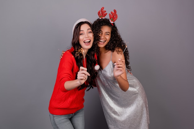 Foto diversas mujeres felices con brillantes bengalas con sombrero de navidad aislado en gris