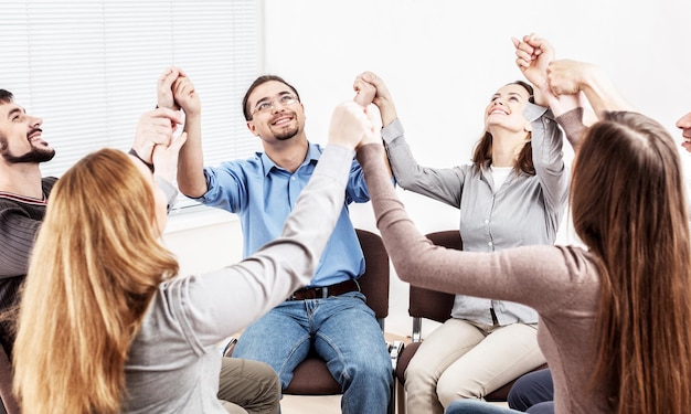 Diversas personas sentadas en círculo cogidos de la mano en la sesión de terapia de grupo,