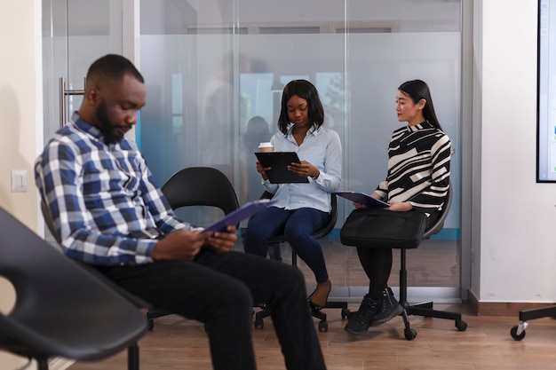 Diversas personas sentadas en el vestíbulo de la empresa de marketing, con currículum vitae mientras esperan ser elegidos para una entrevista. Solicitantes de trabajo multirraciales sentados en la sala de espera de la agencia de investigación.