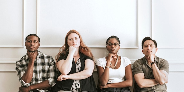 Diversas pessoas mal-humoradas sentadas perto de uma parede branca