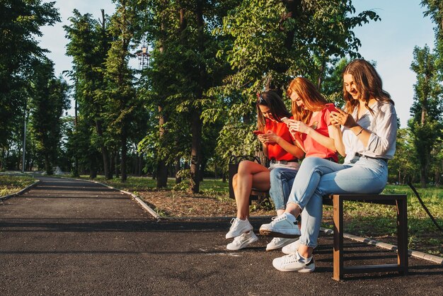 Diverse drei Freundinnen, die ihre Telefone im Freien benutzen, gruppieren gen z junge Leute, die Handys benutzen