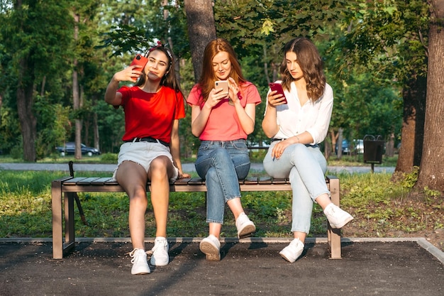 Diverse drei Freundinnen, die ihre Telefone im Freien benutzen, gruppieren gen z junge Leute, die Handys benutzen