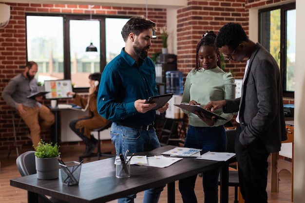 Diverse Geschäftsleute analysieren Marketingstatistiken auf Tablet-Computern, die an einem Unternehmensprojekt im Startup-Büro arbeiten. Multiethnisches Team Brainstorming-Ideen zur Planung der geschäftlichen Zusammenarbeit.