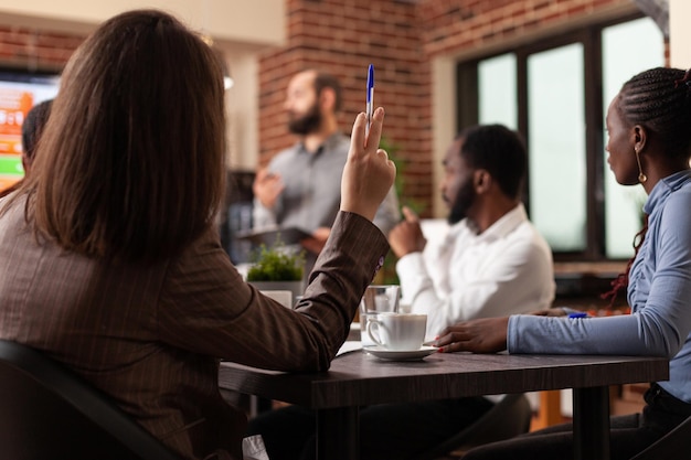 Diverse Geschäftsleute, die an der Management-Präsentation arbeiten, die Unternehmensdiagramme analysieren, die im Startup-Büro arbeiten. Steigende Hand der Geschäftsfrau mit Geschäftsfrage für Partnerschaftsprojekt