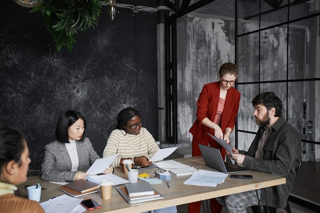 Diverse Geschäftsteams, die das Projekt im schwarzen Bürointerieur diskutieren, konzentrieren sich auf junge Geschäftsfrauen mit roter Jacke, Kopierraum