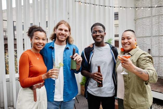 Diverse Gruppe moderner junger Leute, die in die Kamera schauen, während sie sich auf einer Party auf dem Dach im Freien amüsieren