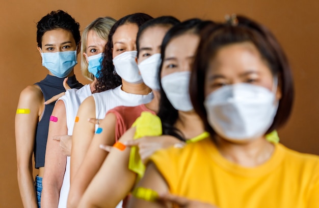 Diverse Gruppe multinationaler ethnischer Patientinnen trägt Gesichtsmasken, die nach der Höhe in einer Reihe stehen.