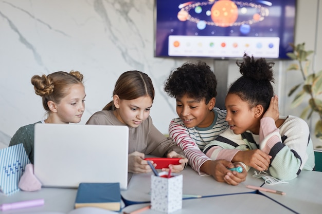 Diverse Gruppe von Kindern, die in der modernen Schule zusammen am Tisch lernen, Platz kopieren