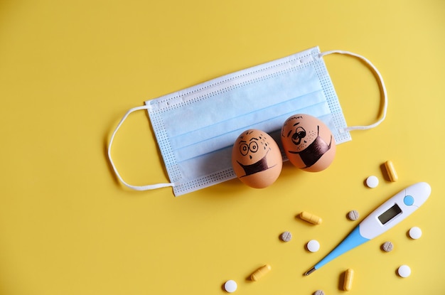 Diverse Hühnereier mit Doodle-Gesichtern, die medizinische Masken auf gelbem Hintergrund tragen. Coronavirus