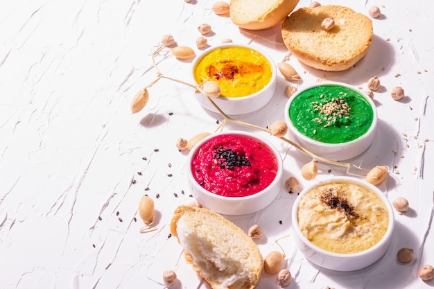 Diverse Hummus-Dips, der flache Hummus in verschiedenen Farben mit Spinat, Rote Beete, Kurkuma und Gemüse, veganer Snack. Weißer Kitthintergrund, Kopienraum