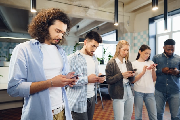 Diverse junge Kollegen, die gemeinsam im Büro an Mobiltelefonen arbeiten