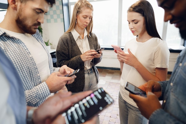 Diverse junge Kollegen, die gemeinsam im Büro an Mobiltelefonen arbeiten