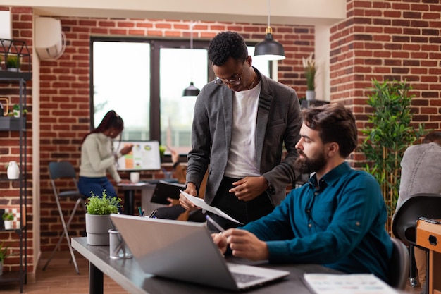 Diverse Unternehmer analysieren Unternehmensgrafiken, die an Marketingprojekten in einem Backsteinmauer-Startup-Büro arbeiten. Multiethnische Geschäftsleute, die über die Strategieplanung für geschäftliche Zusammenarbeit diskutieren