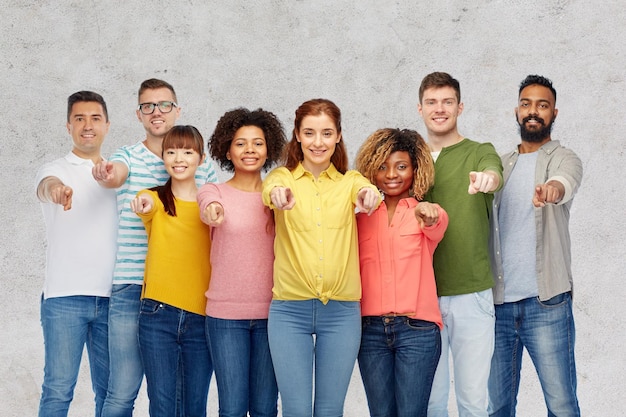 Diversidad, elección, etnia y concepto de personas: grupo internacional de hombres y mujeres sonrientes y felices que le señalan con el dedo sobre un fondo de hormigón gris