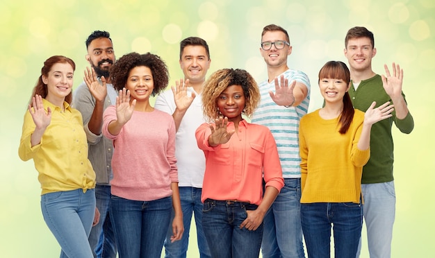 diversidad, raza, etnia y concepto de personas - grupo internacional de hombres y mujeres felices y sonrientes agitando la mano sobre las luces verdes de verano