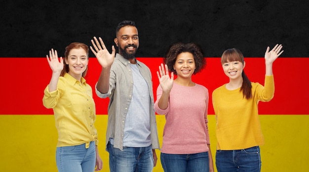 diversidade, imigração e conceito de pessoas - grupo internacional de homens e mulheres sorridentes felizes acenando com as mãos sobre o fundo da bandeira alemã